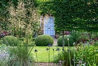 Moleshill garden with a view through Stipa gigantea and pleached trees to topiary box and front door beyond.