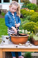 Young girl planting an alpine container garden. Add gravel to improve drainage.