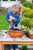 Young girl planting an alpine container garden. Add gravel to improve drainage.
