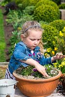 Young girl planting an alpine container garden. Add pebble decoration.