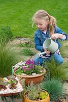 A young girl watering 3 miniature gardens in containers.