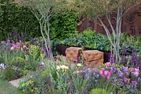 Multi stemmed Amelanchier growing out from gravel path, two oak cube wooden seats, rusted steel fern wall panel, planting of New pink Tulipa 'Caresse', Iris 'Red Zinger' and Iris 'Orange Harvest', Ferns, Hosta, Verbascum and Buxus sempervirens, Hornbeam hedge, Constraining Nature garden - designed by Kate Durr Garden Design - Best Festival Garden award and a gold medal - RHS Malvern spring festival 2015