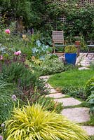 small walled town garden with patio seating area in front espaliered apple trees and gooseberry bushes. In the foreground, a harmoniously cloured mixed border with roses, salvia, rosemary, hackonechloa and Verbena bonariensis.