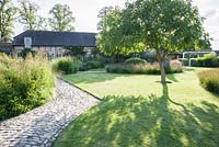 The Courtyard Garden designed by Piet Oudolf and John Coke features several Koelreuteria paniculata, cobble paths and large areas of grasses dotted with flowering plants such as Dianthus carthusianorum and Allium sphaerocephalon. Bury Court Barn, Bentley, Hants, UK
