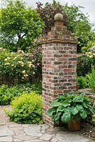 Brick pier constructed from reclaimed materials. Hosta in pot, alchemilla, Rosa 'Buff Beauty' and clematis on garden wall.
