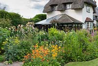 A cottage garden with colourful mixed border of cadelabra primula, achillea, nepeta, paeonia roses 'Fantin Latour' and 'Phyllis Bide' on obelisk, poppies, geranium and foxgloves.