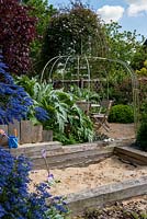 An arbour covered with Clematis montana 'Elizabeth' over a seating area as seen from the children's play area.