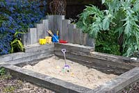 A sand pit and children's play area made from railway sleepers. Behind, grey leaved cardoon and blue ceanothus.