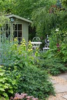 A mixed border of Phlomis russelliana, Thalictrm flavum, ceanothus and clematis in front of a seating area and wooden summer house.