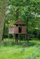 A wooden treehouse sits on stilts in woodland.