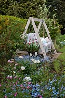 A mixed spring border with Tulipa Purissima, Forget-me-nots and red campion in front of a wooden framed swing seat.