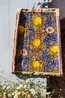 Tile painted with lemons and passionflowers on a door handle with Erigeron karvinskianus growing at its feet - Mexican fleabane - May, Herrenmühle Bleichheim