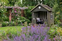 A summer garden with mixed borders including catmint, Rosa 'Gertrude Jekyll' surround a rotating victorian summerhouse.