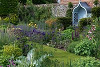 An arbour is tucked away in yew hedging, overlooking perennial borders of bearded iris, aquilegias, geums, lupins and aquilegias.