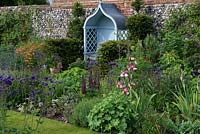An arbour is tucked away in yew hedging, overlooking perennial borders of bearded iris, aquilegias, geums, lupins and aquilegias.