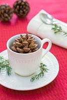 A festive place setting featuring a tea cup with Pine cones and foliage