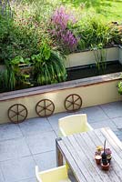 Above view of patio garden showing summer border with water feature, rustic wheels, table and chairs