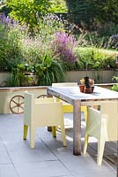 View of patio garden showing summer border, with water feature, rustic wheels, table and chairs