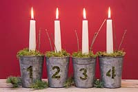 Advent candles in numbered metal pots with moss, against a red background