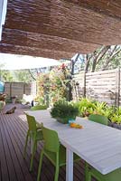 Timber deck with informal dining area and timber panelled screens. Table with potted rhipsalis, green wall screen with assorted bromeliads in background