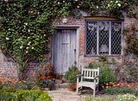 Housefront with climbing rosa, wooden chair and plants in pots and borders, July. The South Cottage, Sissinghurst castle