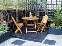 Wooden table and chairs on black timber deck surrounded by hosta and acer, Design Christopher Blandford 'A City Oasis'