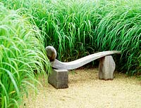 Stylised reclaimed oak bench set in gravel, with background planting of miscanthus sacchariflorus - silver banner grass.  Designer: Anthony Paul. Vineyard Manor, 