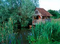 Wildlife pond with waterside planting of bulrushes - scirpus with a wooden boathouse. June, Old Place

