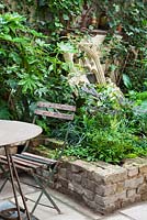 View of raised wall beds with table and chair, church feature and old fire place, Lucille Lewins, small court yard garden in Chiltern street studios, London. Designed by Adam Woolcott and Jonathan Smith 