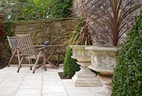Paved seating area featuring cordylines in stone urn planters and box pyramids