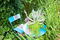 Succulent container on coloured table and chairs. Plants include Agave americana 'Variegata', Echeverias including 'Duchess of Nuremberg' and ice plant Delosperma.