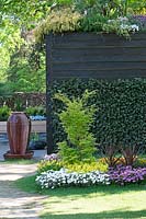 Acer in front of black painted wooden wall with large ceramic pot as fountain. Inspiration garden: Sensory.