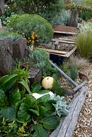 Seaside themed garden with rowing boat, anchor, buoy and driftwood. Santolina, bergenia, stipa, artemisia, Driftwood and Gravel