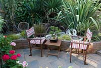 Directors chairs and bonsai on a small table beside raised bed with yucca and phormium, ropes and basket ornaments. Nautical theme.  