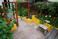 View from above. Hard landscaping stone flooring, yellow painted low walls, timber garden divider creating two rooms and green foliage planting.