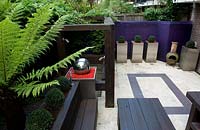 View from above of terrace, wooden furniture and loggia with silver ball water feature, box balls in aluminium containers and in raised bed a tree fern. 