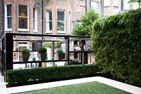 Change of levels in long narrow garden with bamboo hedge, low box hedge and geometric wooden seating area loggia with ornaments.