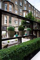 Change of levels in long narrow garden low box hedge and geometric wooden seating area loggia with ornaments.