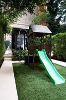 Children's play area with astroturf, slide and playhouse. Garden room building in background