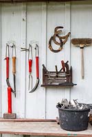 Garden tools and horseshoes arranged on a white painted wooden wall