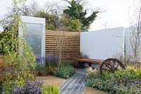 Composite decking by SAiGE lined with Brunnera macrophylla 'Jack Frost' and Nepeta 'Six Hills Giant', leading to a bench with white wall background, Camassia cusickki, Polemonium 'Heaven Scent' - The Low Line, RHS Malvern Spring Festival 2016