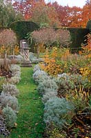 Path edged with santolina leads towards a sundial surrounded by standard honeysuckles at the centre of the Herb Garden at Cranborne Manor Garden, Dorset in autumn