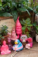 A collection of quirky pink coloured decorative objects in front of a small metal sign, including a Buddha, a duck an owl and two Garden Gnomes.