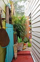 View up side passage of house to garden at back with a blue painted picket fence potted plants and a green garden Gnome statue.