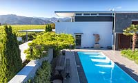 House and swimming pool with mountain range and vineyards beyond at Bhudevi Estate garden, Marlborough, New Zealand.