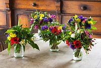 Mixed jam jar arrangements of British grown flowers and foliage - anemone de caen, scented scilly tazetta narcissi, ivy, and viburnum davidii. Common Flower Farm, Somerset