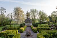 Mitton Manor Garden in spring, Staffordshire. Formal parterre style garden with Neil Wilkin glass scuptures rising from pond