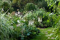 The White Garden.  Grass path with stepping stones, hostas, white metal containers with Astelia and Verbena. Chenies Manor, Buckinghamshire, UK. Late summer. 