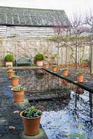 The Canal, framed by pleached limes and terracotta pots, has a wooden seat framed by pots of clipped box at one end. 