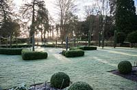 Early morning sun filters through trees to illuminate the formal garden to the south of the house. Welford Park, Newbury, Berks, UK